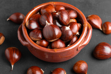 Raw chestnuts into a rustic clay bowl on black backdrop in warm kitchen light
