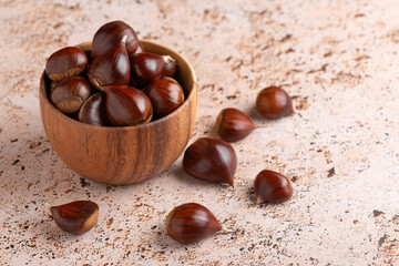 Wooden bowl filled with chestnuts on beige stone kitchen table background, autumnal seasonal food