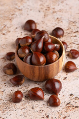 Autumn raw chestnuts in rustic wooden bowl on beige stone kitchen table background, close up