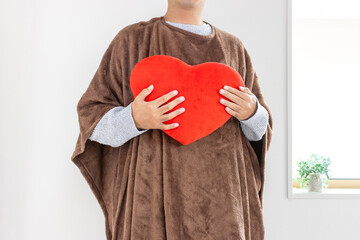 着る毛布を着てハートのクッションを持つ男性（30代、日本人、顔無し）