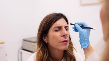 Female beautician in blue gloves marking a patient's face with a white pencil before a cosmetic procedure for wrinkle treatment
