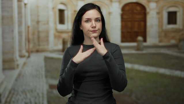 Brunette woman gesturing expressively on university campus with historic architecture in background - Powered by Adobe