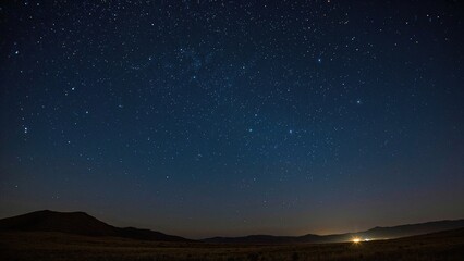 A clear night sky with stars over a landscape with hills and distant light.
