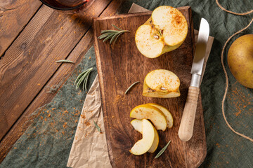 Halved and sliced golden russet apples sprinkled with cinnamon on a dark rustic wooden cutting board with rosemary