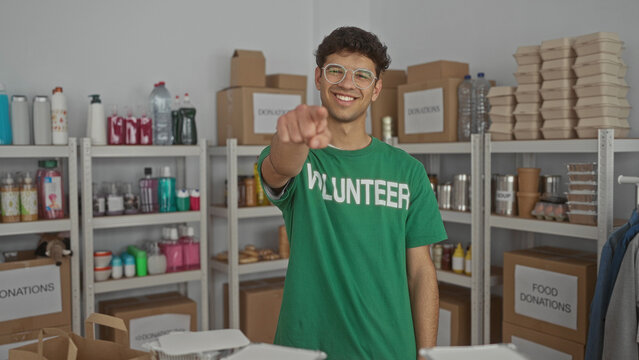 Man smiling and pointing finger to camera in donation center building surrounded by shelves of supplies; compassion service encouragement.