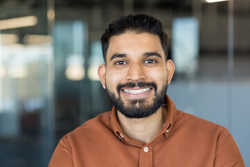 Young indian bearded man smiling confidently, looking towards the camera, standing in a...