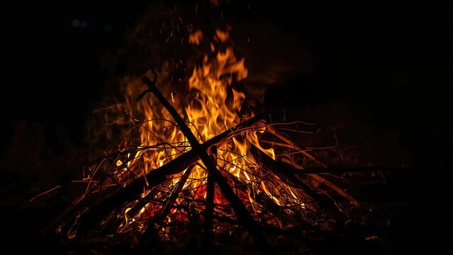 A campfire with burning wood and flames in the dark night.