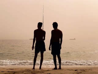Two men fishing on a beach at sunrise