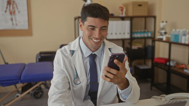 Doctor man in white coat with stethoscope holds smartphone and taps screen at clinic desk; compassion duty. - Powered by Adobe