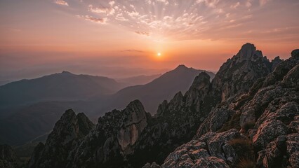 Sunset over mountains from a rocky peak, with warm colors in the sky and rugged terrain in the foreground.