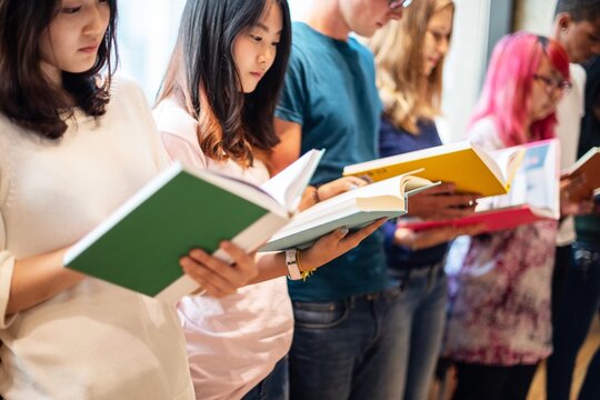 Diverse group reading books. Young adults, mixed ethnicities, focus on reading. Engaged in books, standing in line, diverse readers, enjoying literature together. Diverse young people reading books.