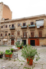 Old European Building Courtyard With Potted Plants, Balconies, And Shuttered Windows In Warm Light Of Day