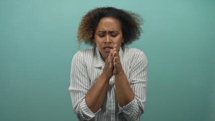 Woman clutching her shoulders and rubbing her hands while shivering against a teal studio backdrop;...