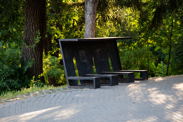 A metal park bench placed along a pathway in a green urban park. The scene features natural greenery and soft daylight, creating a peaceful outdoor atmosphere.