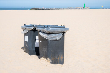 Waste container on beach near blue sea. Trash can in yellow sand.