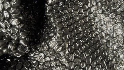 Close-up horizontal video of crumpled black plastic bubble-wrap, showing detailed shiny texture and folds. Ideal for background, overlay, or abstract material footage. - Powered by Adobe