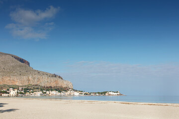 Sunny Beach With Cliffside Village Under Clear Blue Sky By Calm Sea
