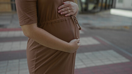 Woman holding her pregnant belly with both hands on a city street pedestrian crossing; anticipation...