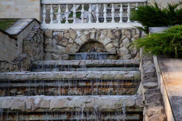 A cascading stone fountain flowing down terrace steps in a peaceful park in Moldova. Surrounded by greenery and overlooking a tranquil lake, this landscape scene captures natural beauty, soft light, a