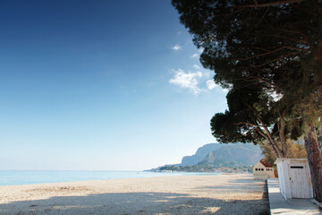 Sunny Beach With Pine Trees, Calm Sea And Mountain Backdrop Under Clear Blue Sky