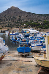 Fototapeta premium The port of the island of Favignana with the traditional wooden fishermen's boats and, in the background, the Castle of Santa Caterina, perched on the top of the hill. Trapani province, Sicily, Italy