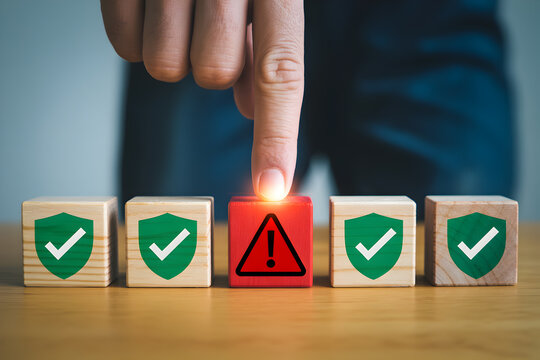 Finger presses red warning block among green checkmark blocks highlighting risk management and cybersecurity concepts on a wooden surface emphasizing potential threats and protection measures