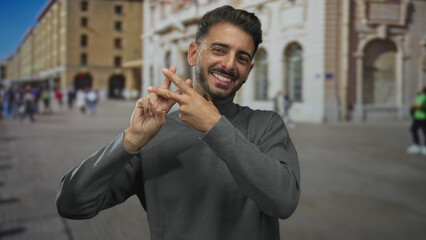 Smiling man in gray turtleneck showing fingers forming hashtag sign on street; digital connectivity.