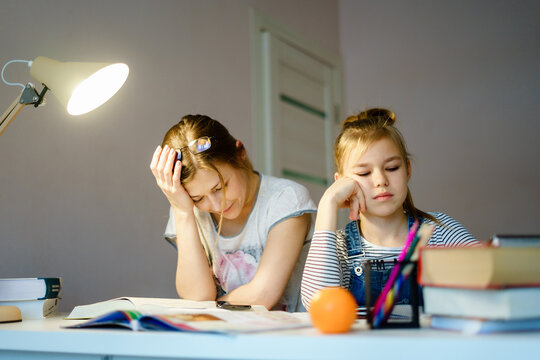 Mother helping her tired daughter with homework at home.