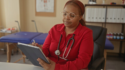 Woman doctor wearing stethoscope writes patient notes on tablet with stylus in office; expertise care focus.