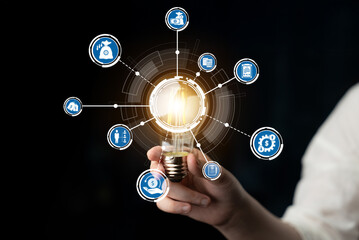 A hand holding a glowing light bulb surrounded by digital icons representing various concepts in business and technology, symbolizing innovation and growth. Crux