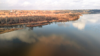 Aerial view of tranquil river landscape in Kazimierz Dolny, surrounded by trees with autumn colors, reflecting clouds on the water surface, showcasing nature's beauty.