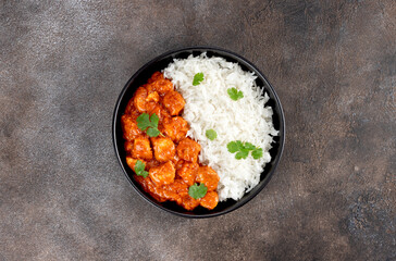 Butter chicken with basmati rice, cilantro in black bowl on gray background. Indian food. Top view.