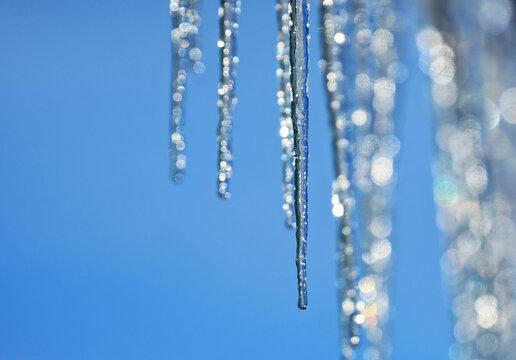 a row of shiny cold icicles dripping and melting on a sunny spring day against a blue sky - Powered by Adobe
