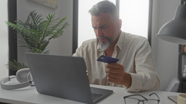 Man holding creditcard at building desk, hand on forehead for headache; online payment frustration debt.