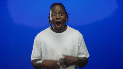 Man with hands on cheeks and open mouth gesturing in studio with blue backdrop; surprise expression energy.