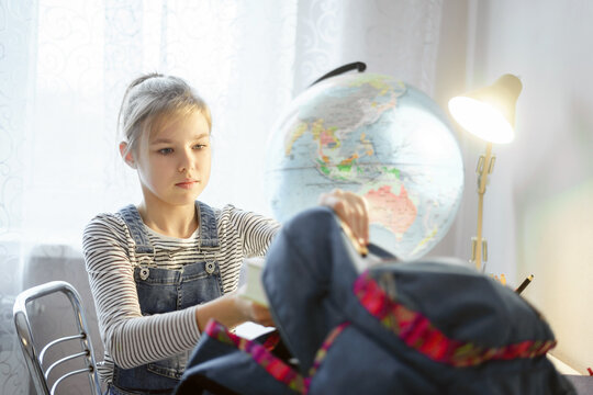 Preteen girl packing stuff in backpack at the table for school after finishing homework