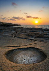 Beautiful sunset over rocky shore with round tide pool in the foreground