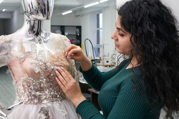 Dressmaker fixing white lace wedding dress on a mannequin in tailor studio
