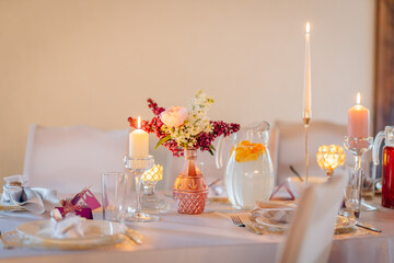 Elegant dining table set for a special occasion, featuring floral centerpiece, candles, and refreshing beverage, creating a warm and inviting atmosphere for guests to enjoy