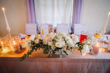 Elegant floral centerpiece arrangement with white roses and greenery on a beautifully set table, surrounded by candles and decorative elements for a festive celebration atmosphere