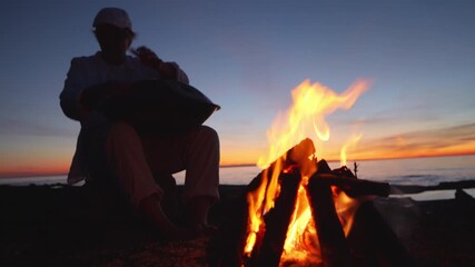 A silhouette of a person meditating by a campfire at sunset, embodying mindfulness and reflection. The serene beach backdrop and warm flames evoke a sense of escape and mental wellbeing.