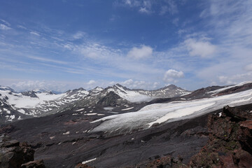 Obraz premium A Majestic View Of A Melting Glacier, Volcanic Slopes, And Snow-Capped Peaks Under A Blue Sky With Clouds.