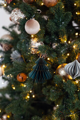 Modern Christmas tree decor featuring paper honeycomb ornaments, velvet baubles, and warm fairy lights on green branches.