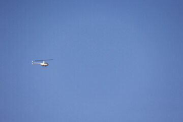 A Minimalist Image Of A Small White Helicopter Flying Alone Against A Vast, Cloudless Blue Sky With Copy Space.