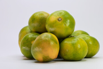 A Heap Of Fresh But Unripe Green And Yellow Tangerines Isolated On A Plain White Surface.