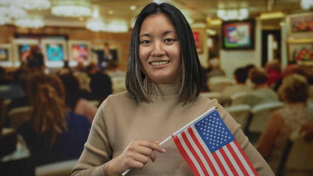 Woman holding american flag smiling in an indoor art gallery, with diverse audience in background, showcasing multicultural enthusiasm and participation in cultural events. - Powered by Adobe
