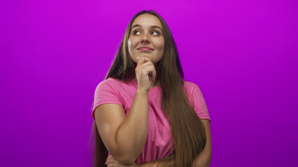 Fototapeta premium Woman with hand on chin in studio with purple backdrop looking up and smiling slightly; thoughtful curiosity.