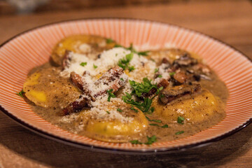 Homemade ravioli with porcini mushrooms and crispy guanciale, served in a creamy sauce and garnished with parsley and parmesan cheese 