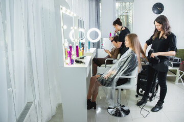 Close up of hairdressers hands drying long blond hair with blow dryer and round brush