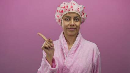 Hispanic woman in a pink bathrobe with a heart-patterned shower cap poses against an isolated pink...
